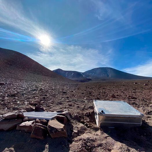 The SO2 camera installation on Lascar Volcano, Chile. The camera is housed inside a protective metal casing, which also holds the battery for powering the instrument; a solar panel for battery charging is located to the left of the box. The SO2 camera installation on Lascar Volcano, Chile. The camera is housed inside a protective metal casing, which also holds the battery for powering the instrument; a solar panel for battery charging is located to the left of the box.