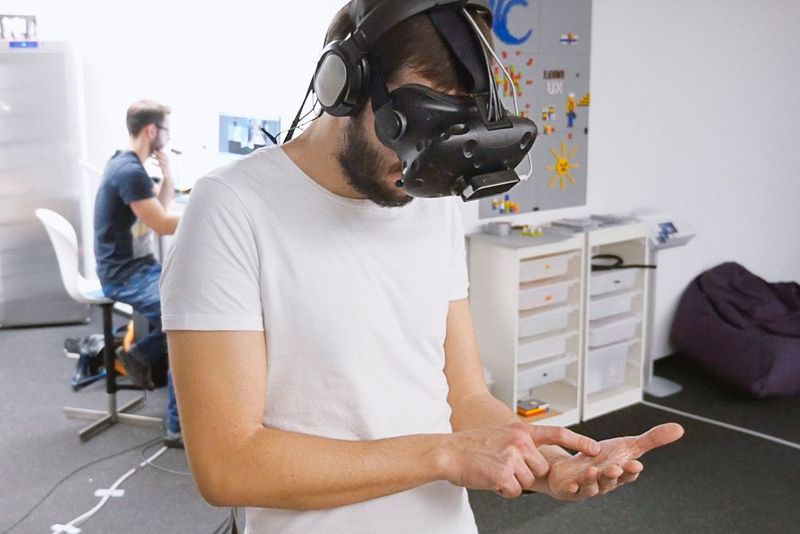 Ein Teilnehmer gibt auf seiner realen Handfläche virtuelle Zahlenwerte ein. Das Experiment wird im Hintergrund von Dominic Gottwalles überwacht. (Universität des Saarlandes)