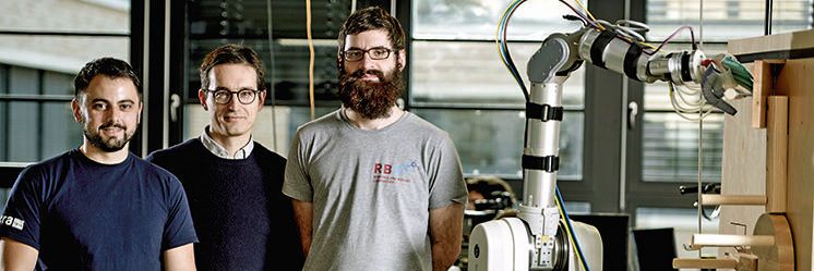 Ein Roboter und sein Entwicklerteam (v. l. n. r.: Roberto Martin Martin, Prof. Dr. Marc Toussaint, Manuel Baum): Bottom-3 steht vor dem Rätsel, eine Klappe durch das Bewegen verschiedener Hebel zu öffnen. Die Forscher wollen herausfinden und nachstellen, wie die Intelligenz von Lebewesen funktioniert.(Bild:  TU Berlin)