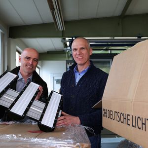 Die neuen dreiflammigen LED-Hallendeckenstrahler werden ausgepackt: Roman Teufl, Geschäftsführer Vertriebsgesellschaft Deutsche-Lichtmiete-Unternehmensgruppe, und Peter Andrä, Geschäftsführender Gesellschafter Riedl Aufzugbau GmbH & Co. KG.