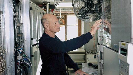 Empa‑Forscher Stefan Reimann auf dem Jungfraujoch vor dem „Medusa“-Messsystem, einem speziell für das AGAGE‑Netzwerk entwickelten Gaschromatograph‑Massenspektrometer, das zahlreiche Spurengase in der Atmosphäre automatisch misst.  (Bild:  Empa)