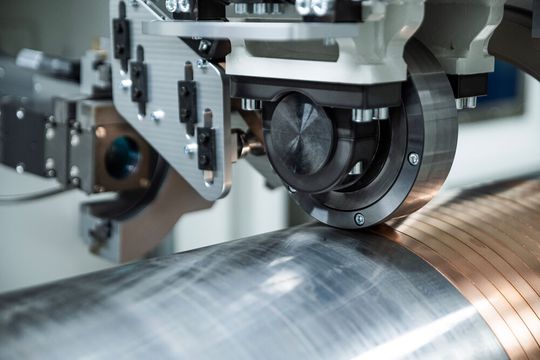 Am Fraunhofer IWS beschichtet man rotationssymmetrische Bauteile mit mehreren Metern Länge jetzt per Metallbandwicklung und Laserenergie. Der neue Prozess heißt Laserdirektplattieren und bringt viele Vorteile im Vergleich zum Laserauftragschweißen ...(Bild:  Fraunhofer IWS)