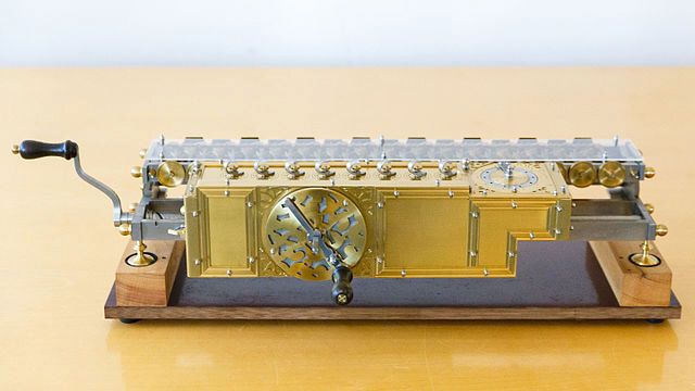 Für seine dezimale Rechenmaschine übertrug Leibniz die einzelnen Lösungsschritte vom schriftlichen Rechnen systematisch auf den mechanischen Vorgang des Zählens, der von zylindrischen Walzen mit jeweils zehn unterschiedlich langen Zähnen in Verbindung mit Zahnrädern ausgeführt wird. Das Bild zeigt einen Nachbau. (Bild:  Rechenmaschine von Leibniz (Nachbau) 05.jpg / Eremeev / CC BY-SA 4.0)