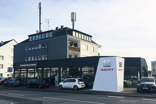 Das Seat-Autohaus an der Lützenkirchener Straße in Leverkusen liegt im Erdgeschoss eines Mehrfamilienhauses. Auffällig ist der „Corner Wall“, ein abgeschrägtes Eckelement mit silbernem Seat-Logo und rotem Schriftzug. (Bild:  Schormann)
