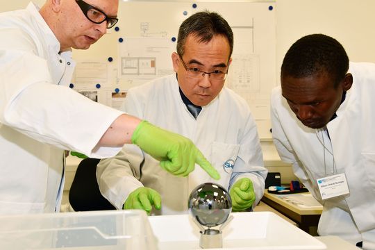 Volker Görlitz (von links) von der PTB zeigt Shih Mean Lee (NMC, Singapur) und Wilson Ombati (KEBS, Kenia) den richtigen Umgang mit der Si-Kugel.(Bild:  PTB)