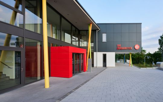 (Tagesklinik in Koblenz: Dem in intensiven „Johanniter Rot“ gehaltenen Eingangsportal der Klinik stellten die Architekten leicht geneigte Stützen in leuchtend bunten Volltönen an die Seite. (Foto: Johanniter))