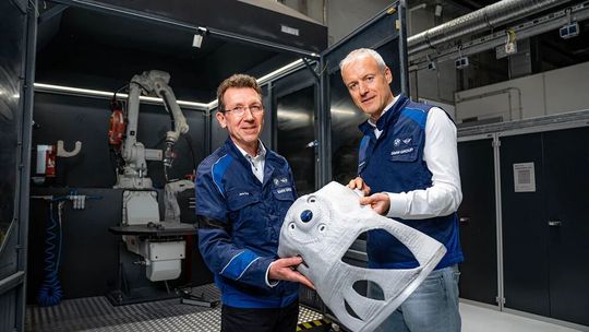 Zwei Spezialisten der BMW Group präsentieren hier ein Aluminiumbauteil, dass durch das additive Fertigungsverfahren Wire Arc Additive Manufacturing (WAAM) hergestellt wurde. Es konnte gezeigt werden, dass die Herstellung im Vergleich zum Druckguss Ressourcen schont.(Bild:  BMW Group)