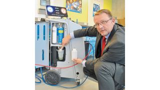 „Low Emisson“ heißt die Waeco-Klimaservice-Technologie, mit der Werkstätten der Umwelt, aber auch ihrem Geldbeutel etwas Gutes tun können. Guido Sasse, Head of Business Development and Marketing bei Waeco, zeigt den dabei zum Einsatz kommenden Altölbehälter, der sich erkennbar von bekannten Modellen unterscheidet. Darüber: die ebenfalls neuartigen Behälter für Frischöl und Kontrastmittel. (Bild: Dominsky)