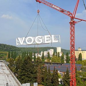 Der neue Schriftzug gelangt per Kran aufs Dach der Vogel Communications Group in Würzburg.