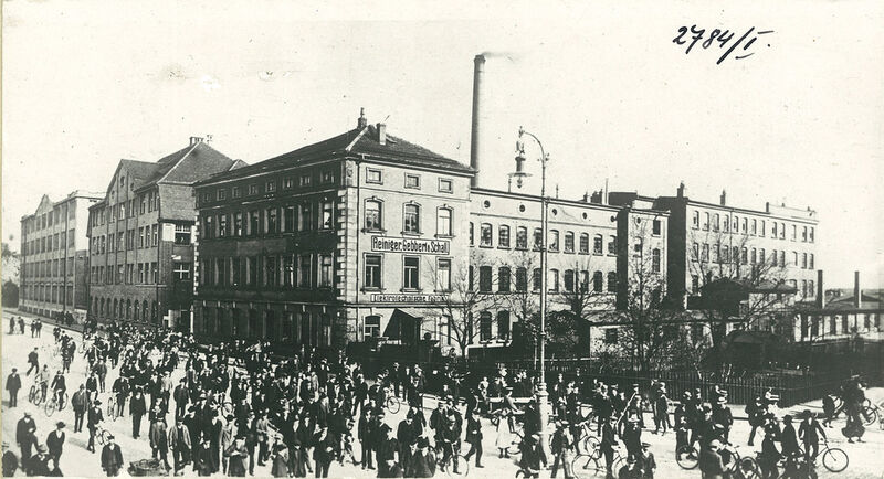 Historische Außenaufnahme (ca. 1920) der Fabrik von Reiniger, Gebbert & Schall (RGS) an der Luitpoldstraße in Erlangen. Das Gebäude wird 1893 bezogen und verfügt über zahlreiche Werkstätten und Büros. Im Vordergrund: Arbeiter verlassen nach Feierabend die Fabrik. (Siemens)