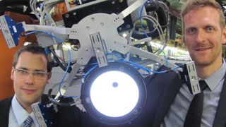 Durch die Integration des Kamerasystems greift der Roboter das Textil immer optimal. Philipp Kosse, Werkzeugmaschinenlabor, WZL (links), und Christoph Greb, Institut für Textiltechnik (rechts) erklären im WZL-Robolab das Konzept. (Bild: RWTH)