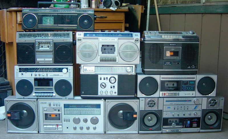 Ebenfalls typisch für die 1980er sind die sogenannten Ghettoblaster: Lauter, immer noch portabler und mit deutlich größeren Leistungsumfang wie zuätzlichen Radiobändern, mehreren Kassettendecks und im Laufe der 1990er Jahre zunehmend auch mit integrierten CD-Playern ausgestattet. (Ghettoblaster-family / Tom Meyer / CC BY 2.0)