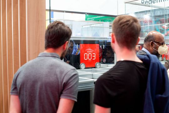 Besucher des Autostore-Messestands während der Logimat 2022 vor einem „Robot“ – der beweglichen Einheit eines Autostore-Kleinteilelagers –, auf dem „Grid“, der das ein- beziehungsweise auszulagernde Gut von oder zur „Workstation“ transportiert.(Bild:  Autostore)