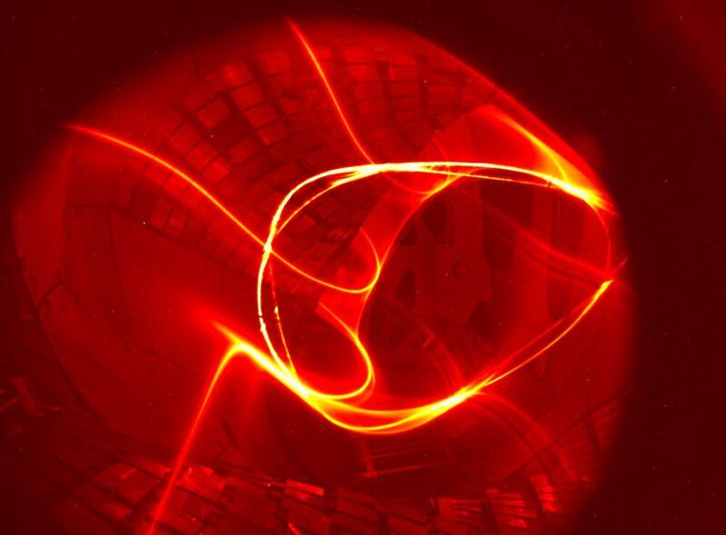 Das Magnetfeld von Wendelstein 7-X (Juli 2015): Das Foto kombiniert die Leuchtspur eines Elektronenstrahls auf seinem vielfachen Umlauf längs einer Feldlinie durch das Plasmagefäß mit den Bildpunkten, die er auf einem fluoreszierenden Stab hinterlässt, der durch die Bildebene geschwenkt wird. (IPP, Matthias Otte)