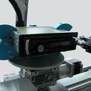 Ein elektrischer Greifer  nimmt im Systec-Messe-Exponat einen Metallstift auf und führt mit diesem verschiedene automatisierte Bedienaktionen am Autoradio aus, etwa das Betätigen des CD-Auswurf-Knopfes.