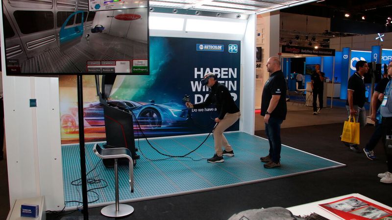 Der Lackierkabinenhersteller Wolf-Anlagentechnik aus Geisenfeld hatte in Zusammenarbeit mit PPG eine offene Lackierkabine aufgestellt, in der Besucher im digitalen Versuch einen Kotflügel lackieren konnten. Ein Anwendungstechniker (rechts) beurteilte dann mit dem Anwender die digitale Lackqualität mittels Schichtdicke, Deckungskraft und Materialverbrauch. (Bild: Jürgen Klasing)