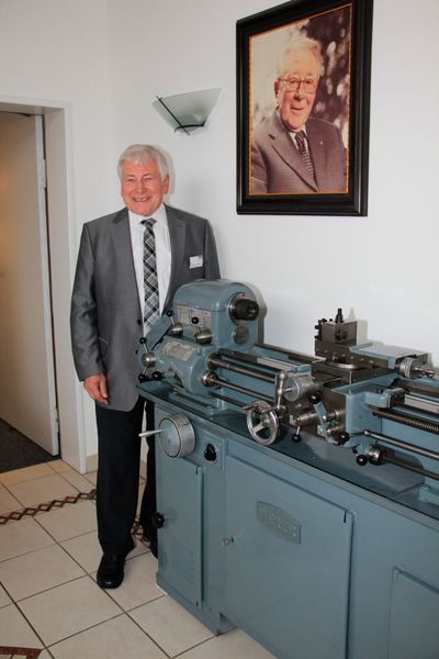 Hermann F. Weiler, Sohn des Firmengründers der Weiler Werkzeugmaschinen und im Anschluss Gründer und Geschäftsführer der GDW Werkzeugmaschinen. Hermann F. Weiler bekleidet zwar kein Amt mehr bei GDW, hat aber bei GDW noch sein eigenes Büro, das Hans Ort extra für ihn vorgesehen hat. Denn selbst als Pensionär treibt ihn die Leidenschaft beihnahe täglich ins Büro. Auf dem Bild steht Hermann F. Weiler vor der Fotografie seines Vaters Friedrich Weiler. (Sonnenberg)