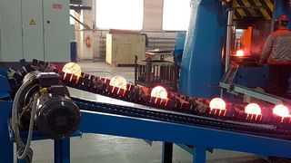 Ein Mitarbeiter entnimmt die geschmiedeten Stahlkugeln von einer Abfuhrrutsche, die im Werkzeugraum integriert ist. (Schuler)