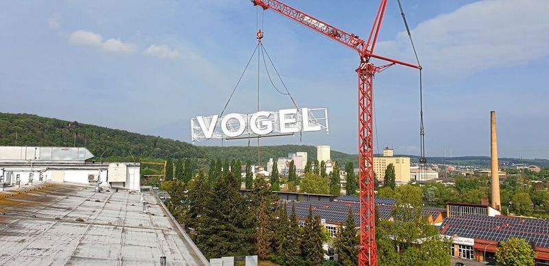 Der neue Schriftzug gelangt per Kran aufs Dach der Vogel Communications Group in Würzburg. (VCG)
