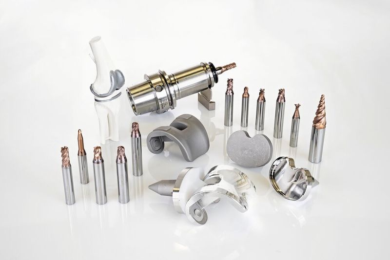 In the middle of the image are the raw parts and the finished knee joint components with a mirrored surface. On the left is the toolset for the upper knee joint implant. On the top right are four tools for the lower knee joint implant as well as additional medical milling tools. (Image:Thomas Entzeroth)