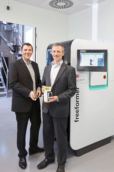 Von links: Die Forscher Sascha Baumann und Dr. Christof Hübner vor dem am Fraunhofer-ICT in Pfinztal installierten Freeformer, mit dem die „Light-Sticks“ gefertigt werden. (Arburg)
