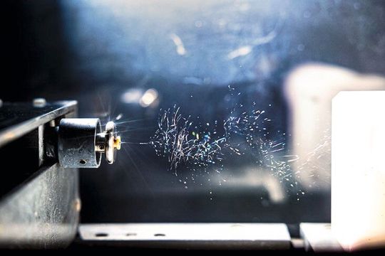 Nahaufnahme des Elektrospinngeräts, mit dem die Kohlenstofffasern hergestellt werden. Links die Nadel, durch die die Polymerlösung gepumpt wird. Die Fasern werden durch ein elektrisches Feld stark in die Länge gezogen und rechts auf dem Kollektor gesammelt.(Bild:  Forschungszentrum Jülich / Sascha Kreklau)