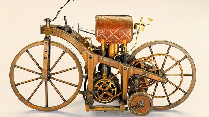Daimlers und Maybachs nächster Schritt nach Erfindung der Standuhr war deren Einbau in ein Fahrzeug. Aus Kostengründen entschieden sie sich für ein hölzernes, mit Stützrädern versehenes Zweirad. Den Rahmen bauten sie aus Hickory-Holz, das mit Eisenplatten verstärkt wurde. Der Motor wurde vertikal zwischen die Holzstützen und Kreuzstreben eingebaut. Über den an einer Scheibe lösbaren Antriebsriemen konnte die Kraft unterbrochen werden. Der Auspuff befand sich unmittelbar unter dem wie ein Reitsattel geformten Ledersitz. Über Schnüre am Lenker konnte die auf das Hinterrad wirksame Klotzbremse betätigt werden. (Bild: Mercedes-Benz)
