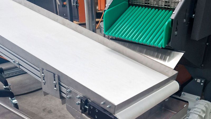 The optional conveyor belt transport system returns the finished work pieces to the loading station where the operator removes them manually. (Source: Rösler Oberflächentechnik)