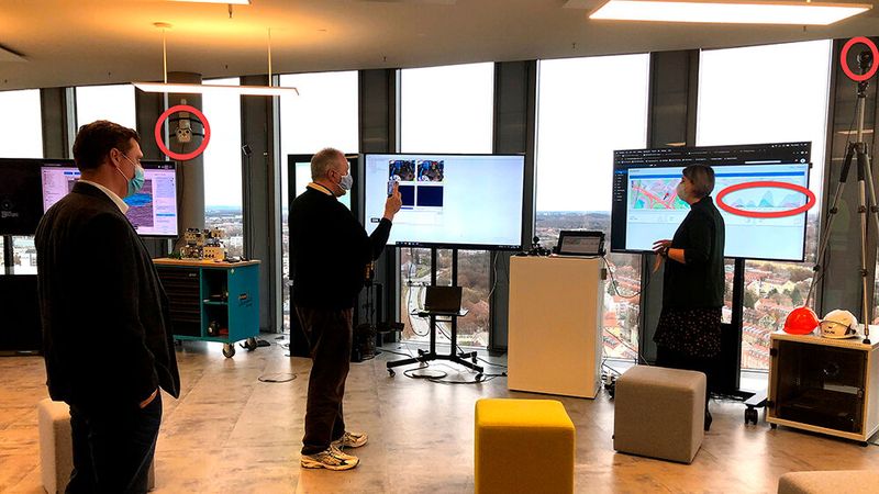 Ebenfalls im November 2020, aber nicht virtuell, sondern echt live bei IBM im 23sten Stock des Watson Center: Zwei Wärmebildkameras (zwei rote Kreise) erkennen Personen mit Fieber, oder Leute ohne Maske. IBM Watson KI zeichnet Analysekurven (rote Ellipse) und gibt lauten Alarm, wenn etwas nicht Corona-kompatibel ist. Leute, von links: Wolfgang Rodler, IBM; Harald Karcher, Journalist; Elena Kotljarowa, IBM. (Bild: Annette Hodapp, IBM)