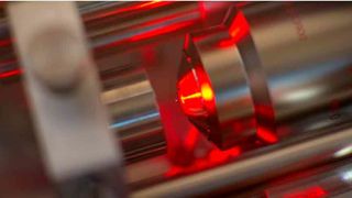 Ein Mikroskop-Objektiv (rechts) bündelt Laserlicht zu einer optischen Pinzette, von der ein Nanokügelchen (winziger roter Punkt in der Bildmitte) in der Schwebe gehalten wird. (Bild: ETH Zürich / Erik Hebestreit und Vijay Jain) (ETH Zürich)