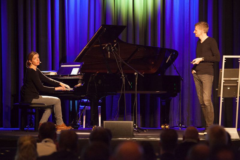 Huldigung – wenn die Pianistin es zulässt: Eva Schüttler demonstriert den Teilnehmern am Steinway-Flügel, wann man bei einem Konzert klatschen „darf“, gemeinsam mit Keynote-Speaker und iTeam-Geschäftsführer Frank Roebers. (Astrid Piethan)