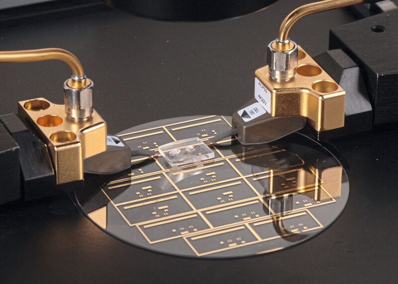 Die Goldlinien auf der Glasscheibe sind Mikrowellenübertragungsleitungen. Der 1,25 cm breite Polymerblock beherbergt eine Miniaturkammer, in der ein mikrolitergroßer Flüssigkeitstropfen erhitzt werden kann. (gemeinfrei)