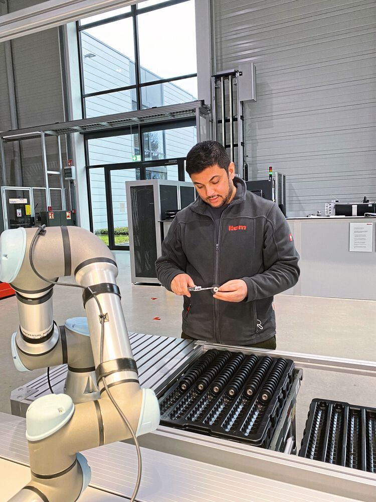 Der Roboter sortiert das fertige Produkt nach der Montage in den Werkstückträger ein. Während der Cobot werkellt, kann sich der Mitarbeitende um andere Aufgaben kümmern.
