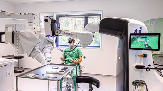 Dr. Maximilian Kückelhaus präsentiert bei einem „Trockentraining“ das neue Verfahren. Der Operationsroboter (links) ist mit einem robotischen Mikroskop (rechts) vernetzt. Dr. Maximilian Kückelhaus präsentiert bei einem „Trockentraining“ das neue Verfahren. Der Operationsroboter (links) ist mit einem robotischen Mikroskop (rechts) vernetzt.