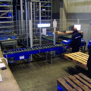 Im automatischen Kleinteilelager bringt ein Regalbediengerät (RBG) das ausgewählte Tablar zur Abgabestation. Dort werden von einem Mitarbeiter die Kleinteile über eine Zählwaage (rechts) entnommen. Anschließend wandert das Tablar wieder zur Abnahmestation, von wo es das RBG zurück ins Regal bringt.