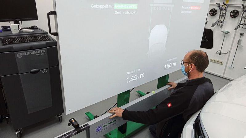 Die Ausrichtung des Kalibriergestells gelingt beim CSC Tool Digital von Hella Gutmann dank Abstandslaser mit Bluetooth-Verbindung deutlich schneller. Eine App projiziert die Werte auf den großen Beamer-Bildschirm.(Bild:  Dominsky/»kfz-betrieb«)