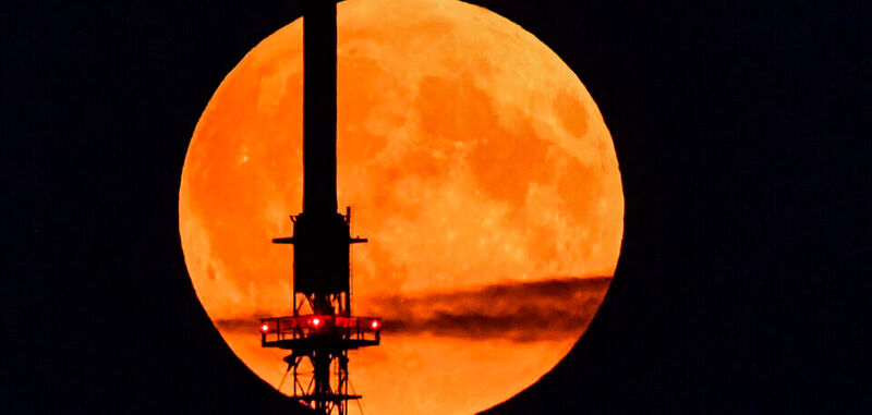 Der rötlich schimmernde Vollmond leuchtet am Abendhimmel hinter einem Funkmast. Wie Nokia meldet ist der finnische Mobilfunkausrüster von der US-Raumfahrtbehörde Nasa auserkoren worden, ein Mobilfunknetz auf dem Mond aufzubauen.