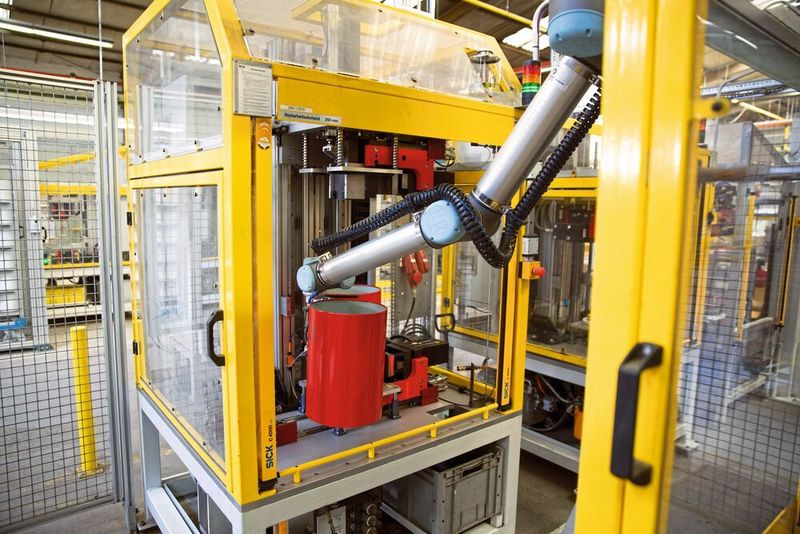 Der UR10 entnimmt einem Klinkautomaten einen gestanzten Blechzylinder, dreht sich um die vertikale Achse und platziert einen unbearbeiteten Rohling in der Maschine. (Universal Robots)