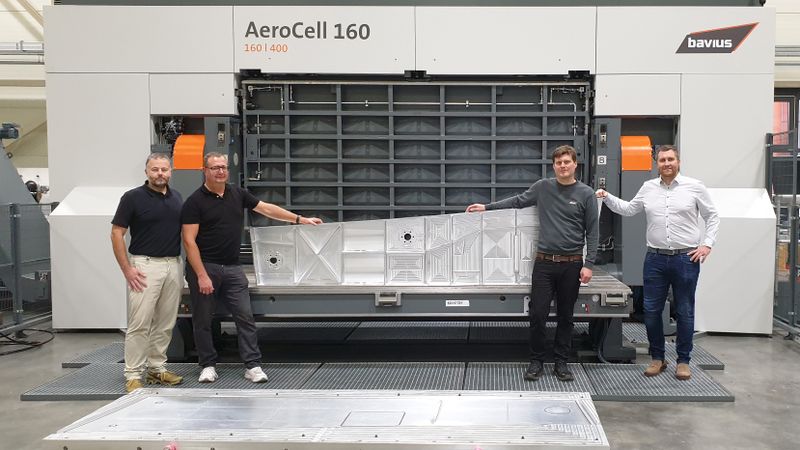 Proudly presenting the finished sample component in front of the AeroCell 160 | 400 (from left): Jens Ilg (Business Development, Aerospace & Composites MAPAL), Alexander Follenweider (Component Manager Aerospace & Composites MAPAL), Stefan Diem (application engineer bavius) and Dominik Merz (Director Global Sales bavius). In the foreground is the fixture used for clamping.(Source:  MAPAL Dr. Kress SE & Co. KG)