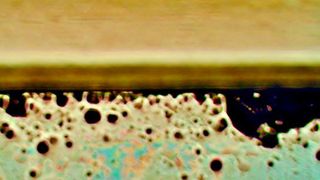 Das Bild zeigt in der Bildmitte die Laminat-Kante. Unterhalb ist der Blick durch den gebondeten Optical Stack mit sichtbar gemachtem Flüssig-Kleber und dessen Eigenschaften: schwarze Stellen zeigen massgeblich Blasenbildung (mehr ist schlechter), beige Stellen in unterschiedlichen Helligkeiten zeigen die Dichte-Verteilung des Klebers und Rot , Grün und Blau in Pastell-Tönen zeigen die Oberflächen-Benetzung und Haftkraft (mehr Farbe ist schlechter).
 (Bild: Wammes und Partner)