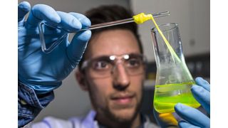 Ein Mitarbeiter zieht im Labor für Systembiotechnologie an der Universität des Saarlandes einen Bionylonfaden aus einem Glaskolben.  (Bild: Silvia Steinbach)