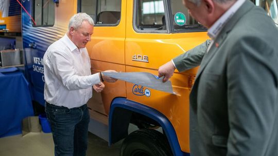 Einweihung von Carli: Geschäftsführer Uwe Schmidt (li.) und Obermeister Michael Schneider von der Innung Sachsen-West enthüllen den neuen Namen des Fahrzeugs.(Bild:  Kfz-Innung Sachsen-West)