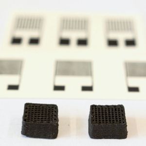 Neuartiger Werkstoff für gedruckte Schaltungen: Zwei Testquader von einem Zentimeter Breite aus dem 3D-Drucker. Im Hintergrund sieht man die gedruckten elektronischen Sensoren.