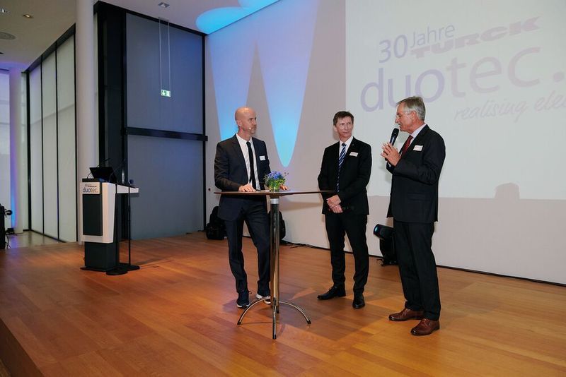 In einer Podiumsdiskussion geben der langjährige Geschäftsführer Eberhard Grünert (r.)  und der derzeitige Geschäftsführer Arthur Rönisch (Mitte) interessante Einblicke in die Unternehmensgeschichte.  (Alexander Ring / Turck Duotec)