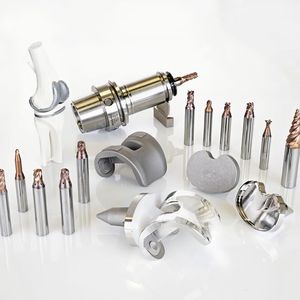 In der Mitte des Bildes die Rohteile und die fertigen Kniegelenk-Komponenten mit spiegelnder Oberfläche. Links der Werkzeugsatz für das obere Kniegelenk-Implantat. Rechts oben sind vier Werkzeuge für das untere Kniegelenk-Implantat sowie weitere medizintechnische Fräser.(Bild:  Thomas Entzeroth)