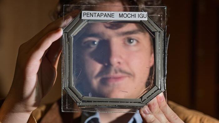 Abram Fluckiger holds up a sample panel square that has five sandwiched layers of a new material nearly transparent insulation material called Mochi, which was designed buy CU Boulder researchers in physics professor Ivan Smalyukh’s lab. (Source:  Glenn J. Asakawa/CU Boulder)