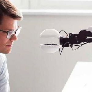 Der Wissenschaftler Marcel Schuck schaut seinen Greifarm an, in der Mitte schwebt ein Kügelchen.