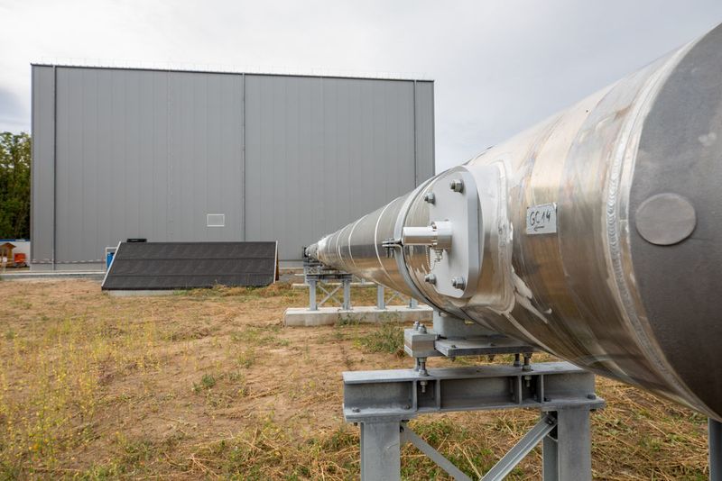 The strand of a gas-insulated cable with a test hall in the background. The outdoor structure is supplied with power from the hall (high voltage, high current and impulse voltages). (Gregor Rynkowski / TU Darmstadt)