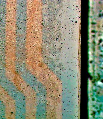 Das Bild zeigt in der Bildmitte die Laminat-Kante. Links ist der Blick durch den gebondeten Optical Stack mit sichtbar gemachtem PSA-Kleber und dessen Eigenschaften: schwarze Stellen zeigen massgeblich Blasenbildung und Partikel-Einschlüsse (mehr ist schlechter), beige Stellen in unterschiedlichen Helligkeiten zeigen die Dichte-Verteilung des Klebers, Rot , Grün und Blau in Pastell-Tönen zeigen die Oberflächen-Benetzung und Haftkraft  (mehr Farbe ist schlechter) und orange/bräunlich zeigen Leiterbahnen eines Touchsensors.   (Bild: Wammes und Partner)