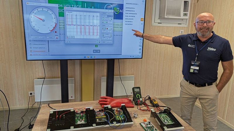 Auf dm Tisch liegt ein kompletter Elektroantrieb mit allen Komponenten – nachgebaut im Kleinformat. 150 Fehlerbilder lassen sich hier einspielen, die mit normalen Diagnosegeräten, den Oszilloskopen oder dem Multimeter gefunden werden müssen.(Bild:  Rosenow – VCG)